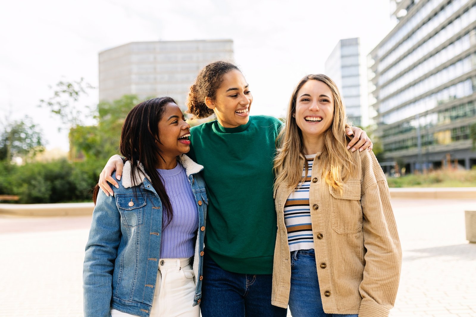 Three happy multiracial young women friends laughing outdoors