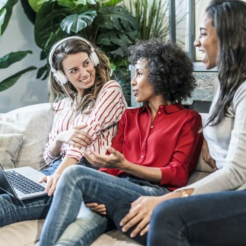Three happy women with laptop sitting on couch