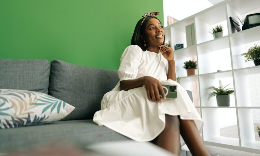 Young african woman sitting on couch at home and using smartphone
